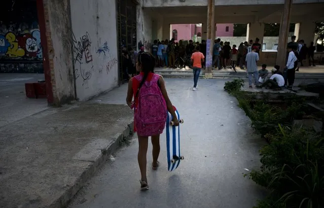 In this January 11, 2018 photo, a young girl carries her Cuba flag motif skateboard to the inauguration ceremony of a new recreational space for skateboarders, created in an abandoned gym at the Educational complex Ciudad Libertad, a former military barracks that the late Fidel Castro turned into a school complex after the revolution in Havana, Cuba. Participants ranged in age from 8 to 50. (Photo by Ramon Espinosa/AP Photo)