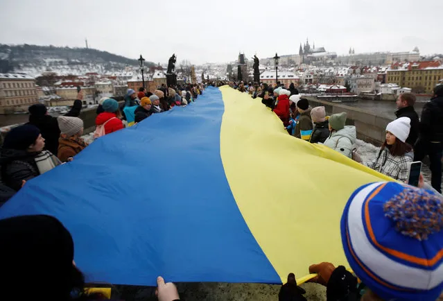 People hold up a giant Ukrainian national flag to mark the Day of Unity of Ukraine at the medieval Charles Bridge in Prague, Czech Republic on January 22, 2023. (Photo by David W. Cerny/Reuters)