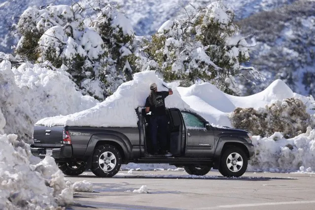 A motorist clears snow from his vehicle as massive amounts of snow trap residents of mountain towns in San Bernadino County, Crestline, California, U.S. March 2, 2023. (Photo by David Swanson/Reuters)