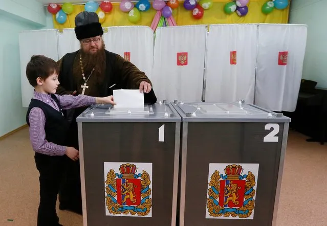 Orthodox priest Sergei Ryzhov and his son Luka cast a ballot at a polling station during the presidential election in the Siberian village of Bolshaya Murta north of Krasnoyarsk, Russia March 18, 2018. (Photo by Ilya Naymushin/Reuters)