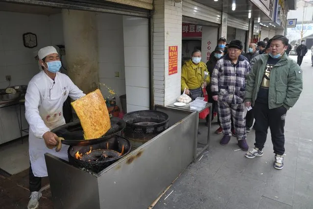 Residents wearing masks to help curb the spread of the coronavirus queue up at a popular food stall in Wuhan, China, Tuesday, January 26, 2021. The central Chinese city of Wuhan, where the coronavirus was first detected, has largely returned to normal but is on heightened alert against a resurgence as China battles outbreaks elsewhere in the country. (Photo by Ng Han Guan/AP Photo)