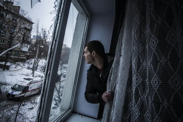Alexander, 35, looks through a broken window of his flat, hit by Ukrainian Army Artillery, in the Voroshilovsky area, center of Donetsk, Ukraine. Sunday, January 18, 2015. The separatist stronghold, Donetsk, was shaken by intense outgoing and incoming artillery fire as a bitter battle raged for control over the city's airport. (Photo by Manu Brabo/AP Photo)