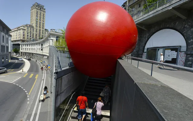 People walk underneath a huge red ball installed   in front of the   Bel-Air  tower as part of the RedBall Project by US artist Kurt Perschke in Lausanne, Switzerland, Monday, July 8, 2013. The RedBall Project is touring Lausanne from July 3 to 9, changing its location every day. (Photo by Laurent Gillieron/AP Photo/Keystone)