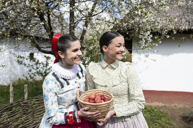 Dressed in folk costumes, female members of the Nyirseg Dance Ensemble hold a basket filled with coloured eggs at the Sosto village museum in Nyiregyhaza, Hungary, 18 April 2022. According to an old Hungarian tradition, on Easter Monday young men pour water on young women, who in exchange present their sprinklers with hand-decorated coloured eggs. (Photo by Attila Balazs/EPA/EFE)