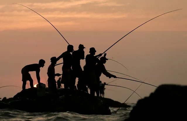 Men hold fishing rods wait for their catch on top of a rock in the sea in Colombo, Sri Lanka on February 10, 2021. (Photo by Dinuka Liyanawatte/Reuters)