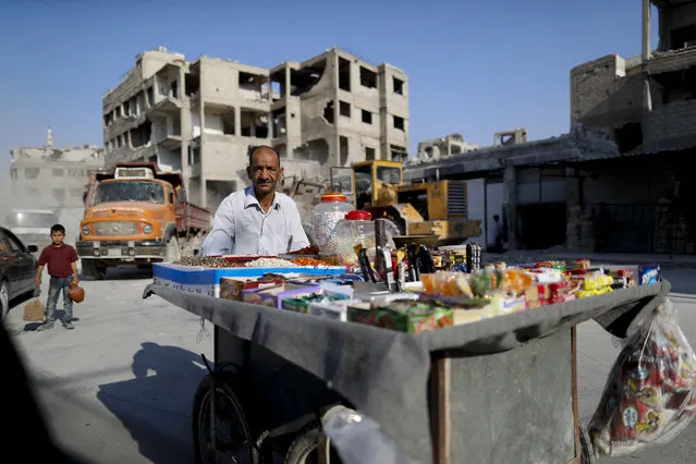 In this Sunday, July 15, 2018, photo, a Syrian man pushes his cart as he sells candies as a bulldozer removes rubble from the town of Douma, in the eastern Ghouta region, near the Syrian capital Damascus, Syria. The celebratory mood in government-controlled areas stems from successive military advances in the past year and an impression that President Bashar Assad, with massive support by unwavering allies Russia and Iran, has won the war or at least militarily defeated the opposition trying to topple him. (Photo by Hassan Ammar/AP Photo)