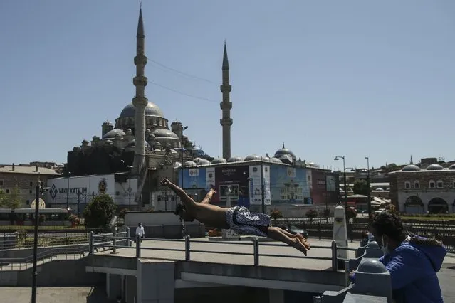 Backdropped by the historical Yeni Cami (New Mosque), a youth jumps from the Galata Bridge into the Golden Horn leading to the Bosphorus Strait separating Europe and Asia, in Istanbul, Friday, May 14, 2021.Turkey is in the final days of a full coronavirus lockdown and the government has ordered people to stay home and businesses to close amid a huge surge in new daily infections. But millions of workers are exempt and so are foreign tourists. Turkey is courting international tourists during an economic downturn and needs the foreign currencies that tourism brings to help the economy as the Turkish lira continues to sink. (Photo by Emrah Gurel/AP Photo)