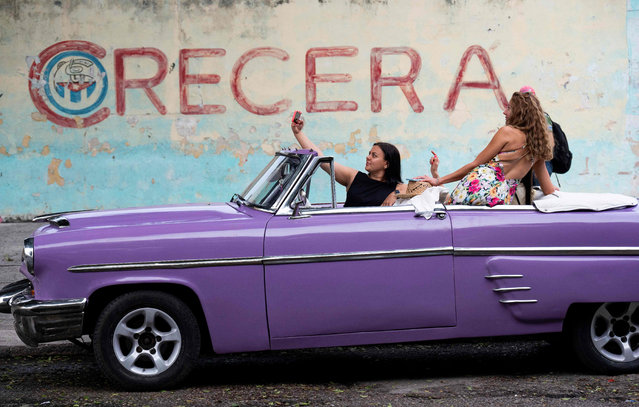 Tourists pose for a selfie in an old American car in front of a wall bearing a graffiti of the Committees for the Defense of the Revolution (CDR) in Havana, on September 27, 2023. September 28 marks the 63th anniversary of the Committees for the Defense of the Revolution (CDR), the so-called “eyes and ears of the Revolution” created by the late Cuban leader Fidel Castro. (Photo by Yamil Lage/AFP Photo)