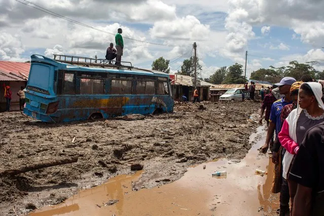 Two men stand on top of a bus as others gather to assess damages at a street covered on mud following landslides and flooding triggered by heavy rainfall in Katesh, Tanzania on December 5, 2023. Torrential downpours in northern Tanzania washed away vehicles and brought down buildings in the hillside town of Katesh, 300 kilometres (185 miles) north of the capital Dodoma. The death toll from landslides and flooding triggered by heavy rainfall in northern Tanzania climbed to 68 on December 4, a regional official said, as rescue workers searched for trapped survivors. (Photo by EEbby Shaban/AFP Photo)
