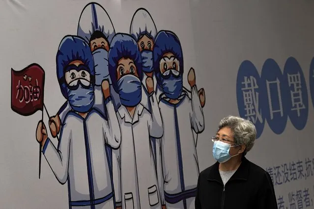 A woman wearing a face mask to help curb the spread of the coronavirus walks by a billboard depicting medical workers flight against the COVID-19 bearing the words “Wear Face Mask” on display along a hutong alley in Beijing, Thursday, October 14, 2021. (Photo by Andy Wong/AP Photo)