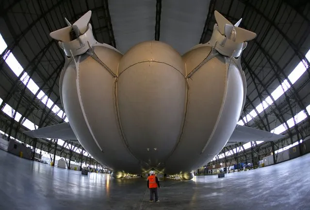 A worker stands under the Airlander 10 hybrid airship during its unveiling in Cardington, Britain March 21, 2016. The world's largest aircraft has been unveiled for the first time since being fully assembled in the UK. The 302ft (92m) long Airlander 10 – part plane, part airship – was floated in a First World War hangar in Bedfordshire. (Photo by Darren Staples/Reuters)