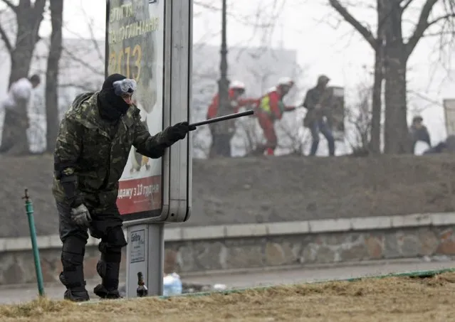 An anti-government protester takes cover behind an advertising board after violence erupted in the Independence Square in Kiev February 20, 2014. (Photo by David Mdzinarishvili/Reuters)