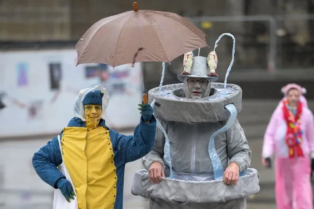 Revellers shelter from the rain under an umbrella as they arrive for the start of the carnival season during the Women's Carnival Day in Cologne, western Germany on February 8, 2024. The festivities begin with “Weiberfastnacht”, a raucous street party in which women snip off men's ties. (Photo by Sascha Schuermann/AFP Photo)