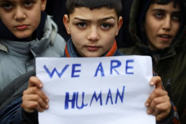 Migrant children hold a sign during a protest outside the transport and logistics centre Bruzgi on the Belarusian-Polish border, in the Grodno region, Belarus on November 25, 2021. (Photo by Kacper Pempel/Reuters)