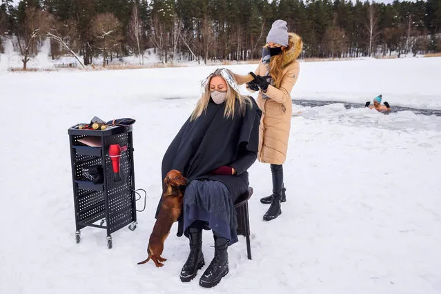 An hairdresser cuts hair on the frozen lake Babelitis while a winter swimmer enjoy swimming in an ice hole on February 15, 2021, in Riga, Latvia, as hairdressers are not allowed to work due to the new coronavirus COVID-19 pandemic. (Photo by Gints Ivuskans/AFP Photo)