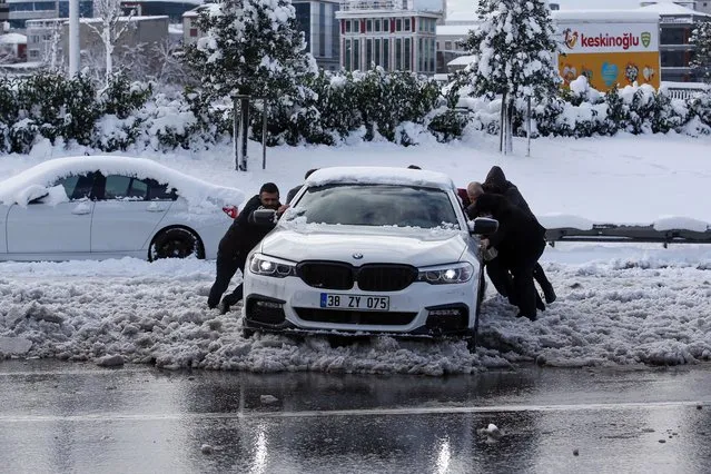 People push a car in a snow-covered street at Istanbul, Tuesday, January 25, 2022. Rescue crews in Istanbul and Athens scrambled on Tuesday to clear throughways that came to a standstill after a massive cold front and snow storms hit much of Turkey and Greece, leaving countless people and vehicles in both cities stranded overnight in freezing conditions. (Photo by Emrah Gurel/AP Photo)