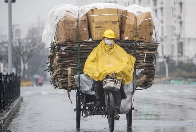 A worker wearing rain protection steers his tricycle packed with recycling papers in Shanghai on March 13, 2017. (Photo by Johannes Eisele/AFP Photo)