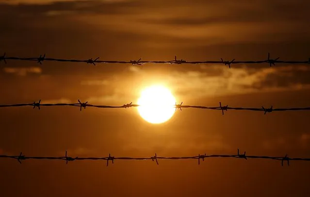 The sun rises behind barbed wire at the airport terminal on the Greek island of Santorini, Greece, July 1, 2015. (Photo by Cathal McNaughton/Reuters)