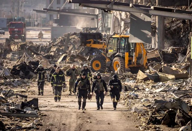 Ukrainian firefighters work amid the rubble of the Retroville shopping mall, a day after it was shelled by Russian forces in a residential district in the northwest of the Ukranian capital Kyiv on March 21, 2022. At least six people were killed in the bombing. Six bodies were laid out in front of the shopping mall, according to an AFP journalist. The building had been hit by a powerful blast that pulverised vehicles in its car park and left a crater several metres wide. (Photo by Fadel Senna/AFP Photo)