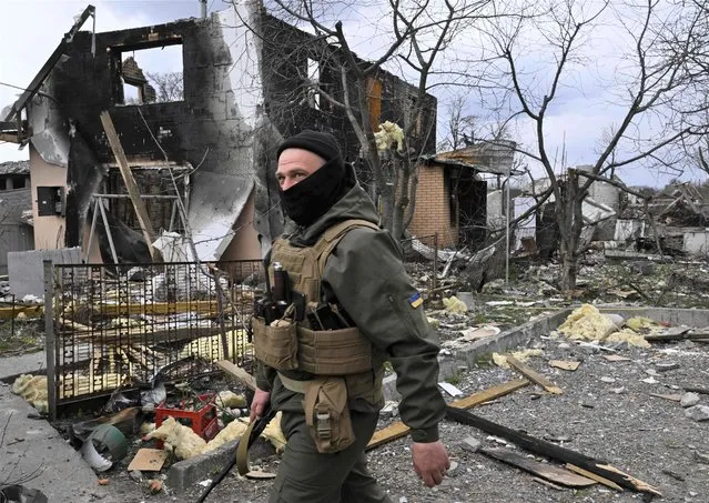 A member of the Ukrainian territorial defense forces walks in front of a destroyed house in Bohdanivka village, northeast of Kyiv, on April 12, 2022. While Russia appears to have abandoned for now its aim of pushing deep into the heart of Ukraine, its new declared goal of taking control of much of the east of the country still risks a protracted and bloody conflict. (Photo by Genya Savilov/AFP Photo)
