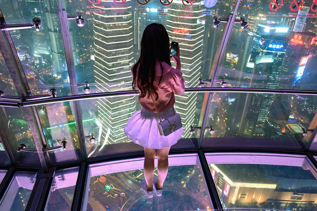 A young woman takes pictures of the city with her mobile phone, from the glass-floor observation platform, in the Oriental Pearl Tower, in the financial district of Shanghai, on May 9, 2019. (Photo by Hector Retamal/AFP Photo)