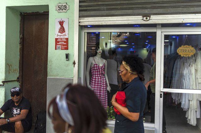 Residents walk past a closed, private clothing store in Havana, Cuba, Saturday, November 11, 2023. (Photo by Ramon Espinosa/AP Photo)