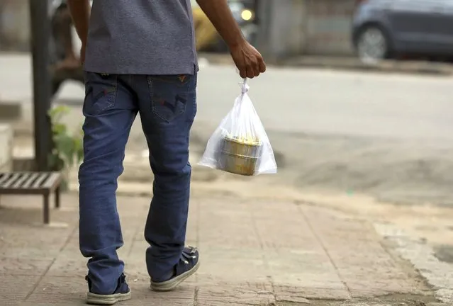 A man carrying his tiffin box in a single use plastic cover walks through a street in Hyderabad, India, Thursday, June 30, 2022. India banned some single-use or disposable plastic products Friday as a part of a longer federal plan to phase out the ubiquitous material in the nation of nearly 1.4 billion people. (Photo by Mahesh Kumar A./AP Photo)