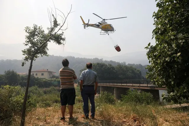 People watch as a helicopter works on containing a wildfire at Garganta de los Infiernos natural reserve, during the second heatwave of the year, in Jerte, Spain on July 17, 2022. (Photo by Isabel Infantes/Reuters)