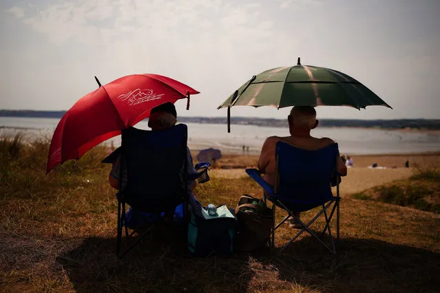 People sheltering under umbrellas from the sun in St Michael's Bay in Cornwall, England, Sunday July 17, 2022. The Met office has issued its first-ever “red warning” of extreme heat for Monday and Tuesday, when temperatures in southern England may reach 40 C (104 F) for the first time. (Photo by Ben Birchall/PA Wire via AP Photo)