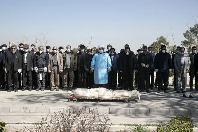Mourners wearing face masks and gloves pray over the body of former politburo official in the Revolutionary Guard Farzad Tazari, who died Monday after being infected with the new coronavirus, at the Behesht-e-Zahra cemetery just outside Tehran, Iran, Tuesday, March 10, 2020. Iran is the hardest-hit country in the Mideast by the new coronavirus, which sickens but largely doesn't kill those afflicted. (Photo by Mahmood Hosseini/Tasnim News Agency via AP Photo)