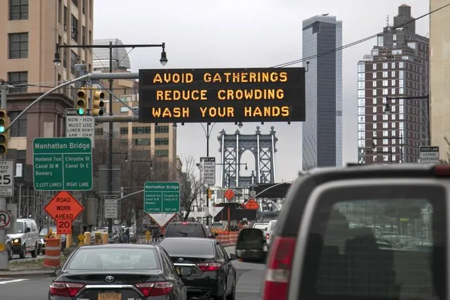 The Manhattan bridge is seen in the background of a flashing sign urging commuters to avoid gatherings, reduce crowding and to wash hands in the Brooklyn borough of New York, on Thursday, March 19, 2020. In a matter of days, millions of Americans have seen their lives upended by measures to curb the spread of the new coronavirus. For most people, the new coronavirus causes only mild or moderate symptoms. For some it can cause more severe illness. (Photo by Wong Maye-E/AP Photo)
