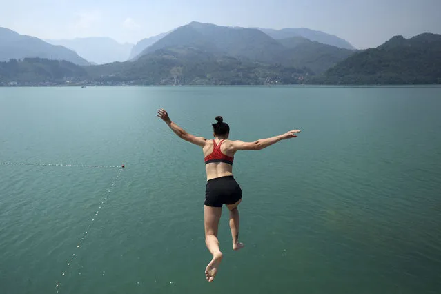 Damira jumps in the Jablanicko lake water in Lisicici, Bosnia, Sunday, July 24, 2022. Mountains around the lake are blanketed by smoke from wildfires currently raging on the nearby mountain Cvrsnica as hot weather sets in with temperatures rising up to 40 degrees Celsius (104F). (Photo by Armin Durgut/AP Photo)