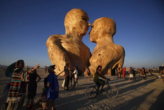 People gather around the art installation Embrace during the Burning Man 2014 “Caravansary” arts and music festival in the Black Rock Desert of Nevada August 26, 2014. People from all over the world have gathered at the sold out festival to spend a week in the remote desert cut off from much of the outside world to experience art, music and the unique community that develops. (Photo by Jim Urquhart/Reuters)
