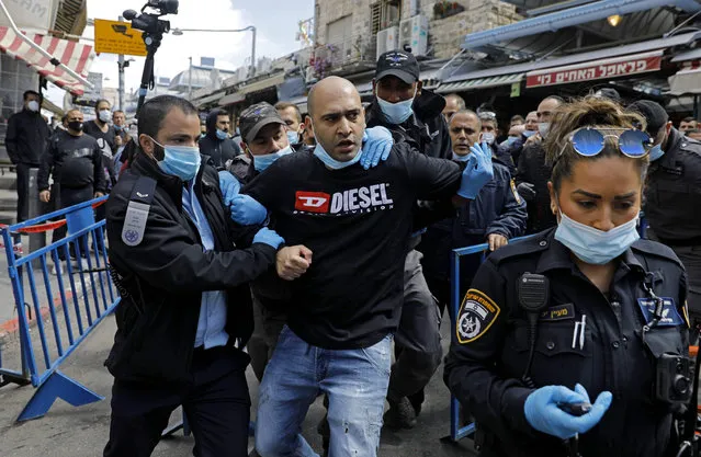 Israeli policemen wearing protective face masks, arrest a merchant in Jerusalem's Mahane Yehuda market, on April 26, 2020, during scuffles between security forces and protesters, angry about the continued closure of the landmark open air market, after authorities reduced some lockdown measures imposed in order to stem the spread of the novel coronavirus, by allowing shops to reopen. (Photo by Menahem Kahana/AFP Photo)