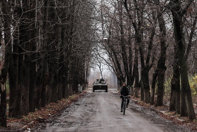 A man cycles as a military infantry vehicle drives through Chasiv Yar, near the frontline in the Donetsk region, Ukraine, 09 November 2023, amid the Russian invasion. Russian troops entered Ukrainian territory in February 2022, starting a conflict that has provoked destruction and a humanitarian crisis. (Photo by Oleg Petrasyuk/EPA/EFE)