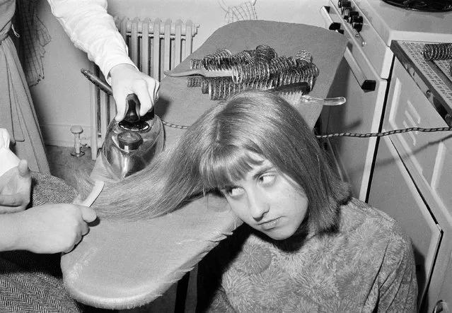 Teenage girls are all steamed up these days about straight hair. The steam iron is replacing the huge rollers on which countless teens slept every night to achieve the height and curls fashionable until. The same girls endure having their hair stretched to absolute straightness on the ironing board, and then ironed to keep it that way. Unlike the roller setting, this takes teamwork. Gay Stilley, 14, goes through an ironing session with a couple of her friends at the Stilley Home in Glen Oaks, Queens, New York City on December 23, 1964. With a wary eye, Gay tries to watch the straightening process as one friend stretches her hair with a comb and another does the ironing, in the Stilley kitchen. (Photo by Marty Zimmerman/AP Photo)