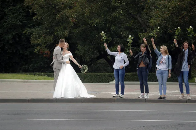 A newly wed couple kiss as Belarusian opposition supporters hold flowers during a protest in Minsk, Belarus, Thursday, August 20, 2020. Demonstrators are taking to the streets of the Belarusian capital and other cities, keeping up their push for the resignation of the nation's authoritarian leader. President Alexander Lukashenko has extended his 26-year rule in a vote the opposition saw as rigged. (Photo by Dmitri Lovetsky/AP Photo)