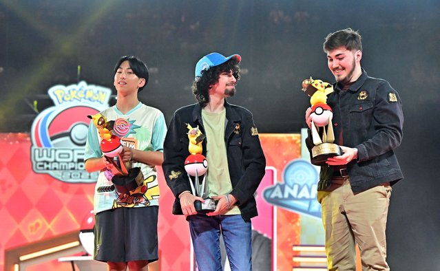 Kevin Han (L), Senior division champion, and James Evans (C), Masters finalist, watch as Giovanni Cischke (R), Masters champion, inspects his trophy at the Pokémon World Championships in Anaheim, California, on August 17, 2025. Han became the first player to win world titles in two different age divisions after claiming the Juniors crown in 2024. (Photo by Frederic J. Brown/AFP Photo)