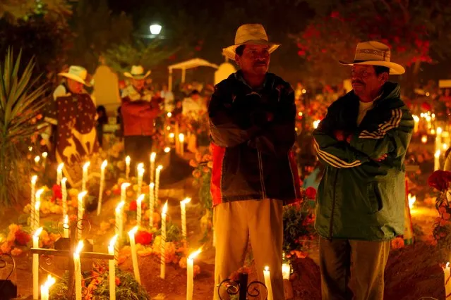 Men stand next to the graves of their relatives on the Day of the Dead, at a cemetery in Santa Maria Atzompa, on the outskirts of Oaxaca, November 1, 2015. Mexicans mark the Day of the Dead by paying homage to their dead relatives, through the decoration of their graves, and the preparation of meals. (Photo by Lorenzo Hernandez/Reuters)