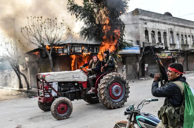 A Turkish-backed Syrian rebel drives past a burning shop in the city of Afrin in northern Syria on March 18, 2018. Turkish forces and their rebel allies were in control of the Kurdish-majority city of Afrin in northwestern Syria, AFP journalists on the ground reported. (Photo by Bulent Kilic/AFP Photo)