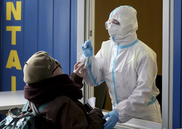 A medical worker, right, tries to test woman for COVID-19 in a set up for rapid new coronavirus testing in Vienna, Austria, Monday, November 30, 2020. The Austrian government has moved to restrict freedom of movement for people, in an effort to slow the onset of the COVID-19 disease and the spread of the coronavirus. (Photo by Ronald Zak/AP Photo)
