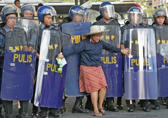 A woman stands in front of policee as Filipino laborers clash with police in the Makati section of Manila on November 16, 2015 during protests to raise issues as world leaders arrive for the Asia-Pacific Economic Cooperation (APEC) Summit this week. APEC members account for 57 percent of the global economy and 40 percent of the world's population, with the diverse grouping including Papua New Guinea, Peru, Japan and Russia. (Photo by Joseph Agcaoili/AFP Photo)