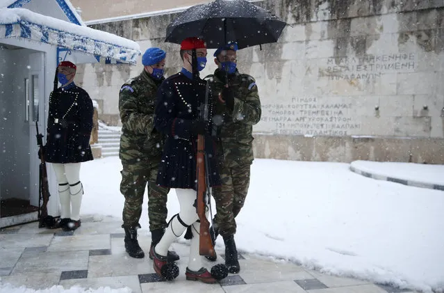 Soldiers help a member of the Presidential Guard, known as Evzonas, during the changing of the guard as snow falls at the tomb of the Unknown Soldier in Athens, Tuesday, February 16, 2021. A cold weather front has hit Greece, sending temperatures plunging from the low 20s Celsius (around 70 Fahrenheit) on Friday to well below freezing on Tuesday, and heavy snowfall in central Athens. (Photo by Thanassis Stavrakis/AP Photo)