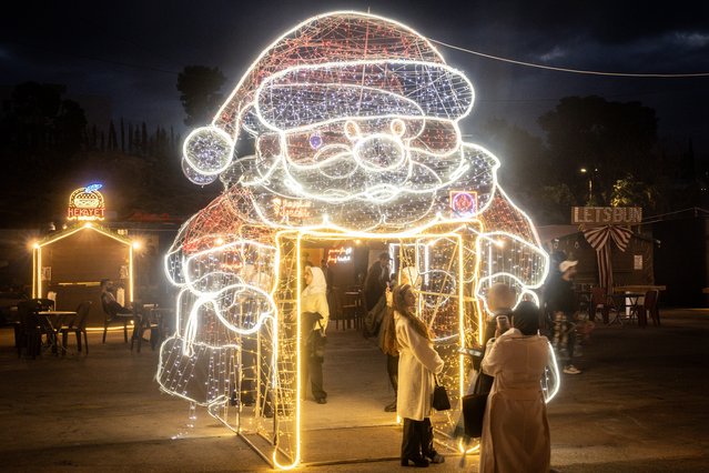 A woman poses for a photograph underneath a Santa Claus light display at the Damascus Christmas market on December 22, 2024 in Damascus, Syria. On December 8, rebel forces in Syria retook the capital and several other cities from longtime ruler Bashar al-Assad, who fled the country for Moscow. The fall of the Assad regime marks a new chapter for Syria, which has been mired in a multi-party civil war since 2011, sparked by the Arab Spring uprisings. (Photo by Chris McGrath/Getty Images)