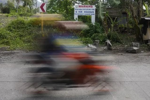 Residents on motorcycle pass by a warning sign at Bonga village, Albay province, northeastern Philippines, on June 10, 2023. Thousands of poor Filipinos risk their lives by living and working in villages inside a permanent danger zone around Mayon volcano. (Photo by Aaron Favila/AP Photo)