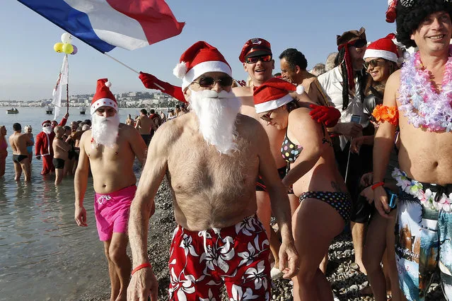 People wearing swimsuits, Christmas hats, and holding a French flag, attend the traditional Christmas on December 20, 2015 on the beach of the French riviera city of Nice, southeastern France. (Photo by Valery Hache/AFP Photo)