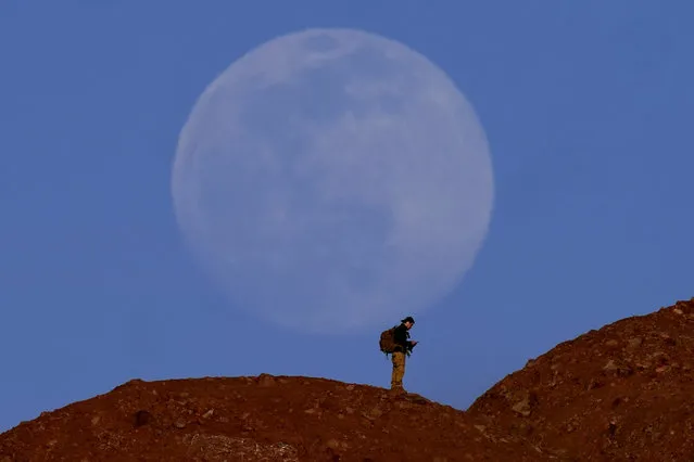 The nearly-full moon rises beyond a hiker at Papago Park on Thursday, February 25, 2021, in Phoenix, Arizona. (Photo by Charlie Riedel/AP Photo)