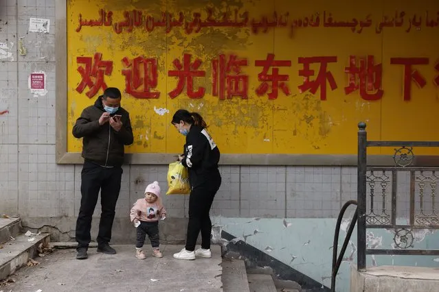 A family stands at the entrance to an underground retail street in Aksu in western China's Xinjiang Uyghur Autonomous Region on March 18, 2021. (Photo by Ng Han Guan/AP Photo)