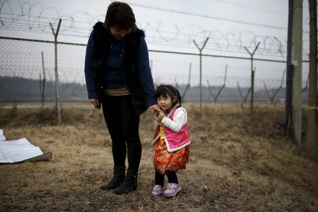 A girl dressed in a Hanbok, a Korean traditional costume, holds her mother's hand in front of a barbed-wire fence, after a memorial service for North Korean family members, near the demilitarized zone separating the two Koreas, in Paju, February 8, 2016, on the occasion of Seolnal, the Korean Lunar New Year's day. Millions of South Koreans travelled to their hometowns during the three-day holiday. Seolnal is one of the traditional holidays when most Koreans visit their hometowns to be united with their families and hold memorial services for their deceased ancestors. (Photo by Kim Hong-Ji/Reuters)