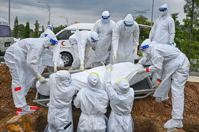 Volunteers wearing protective suits lay down the body of a Covid-19 coronavirus victim for burial at the Raudhatul Sakinah Muslim cemetery in Kuala Lumpur on June 15, 2021. (Photo by Mohd Rasfan/AFP Photo)